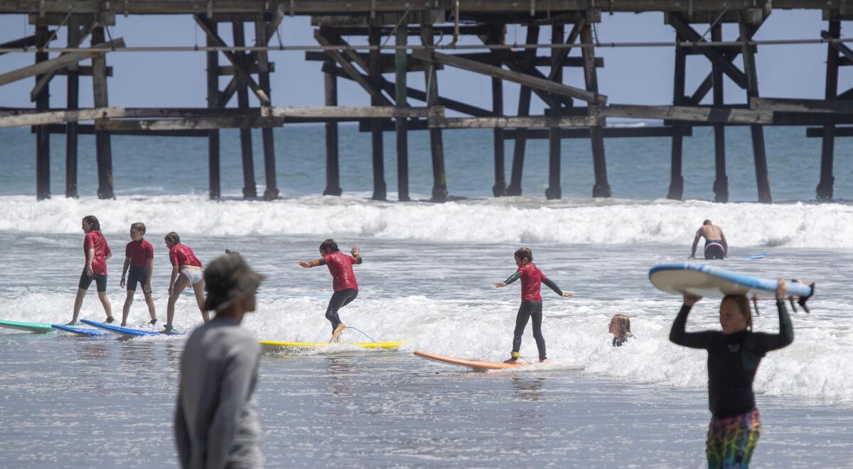 Kids ride a wave together as they learn to surf on a summer day at the San Clemente Pier Tuesday.