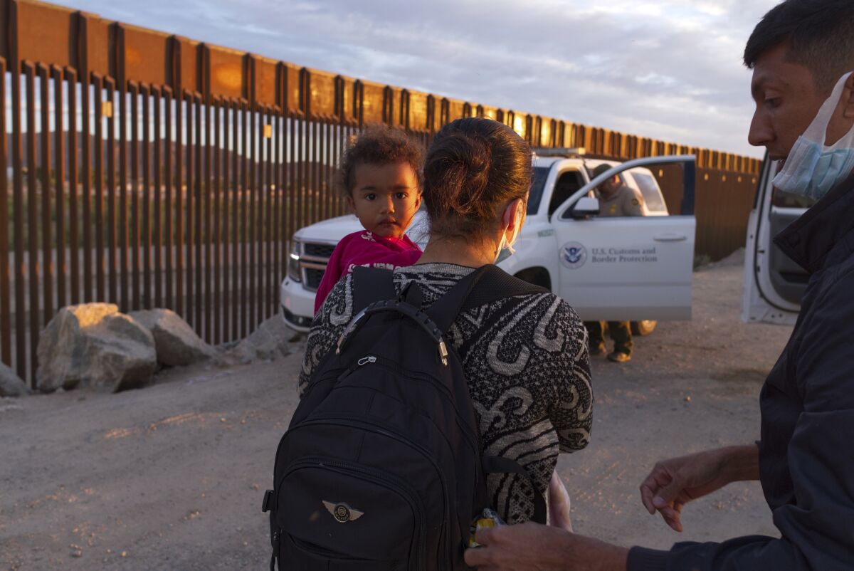 A woman carries a baby near the border wall.