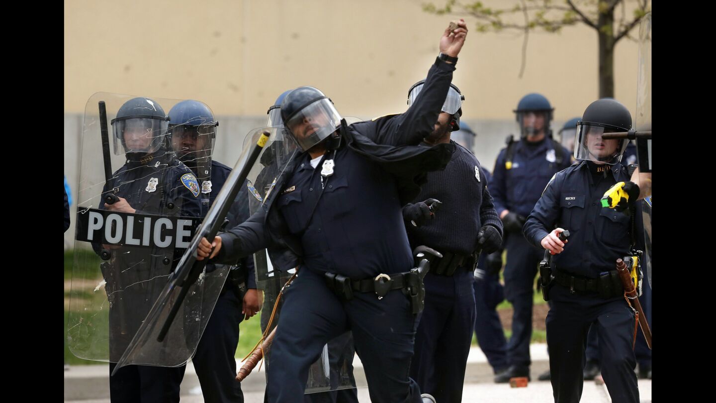 A Baltimore police officer throws a rock back at protesters outside the Mondawmin Mall after the funeral of Freddie Gray on Monday.
