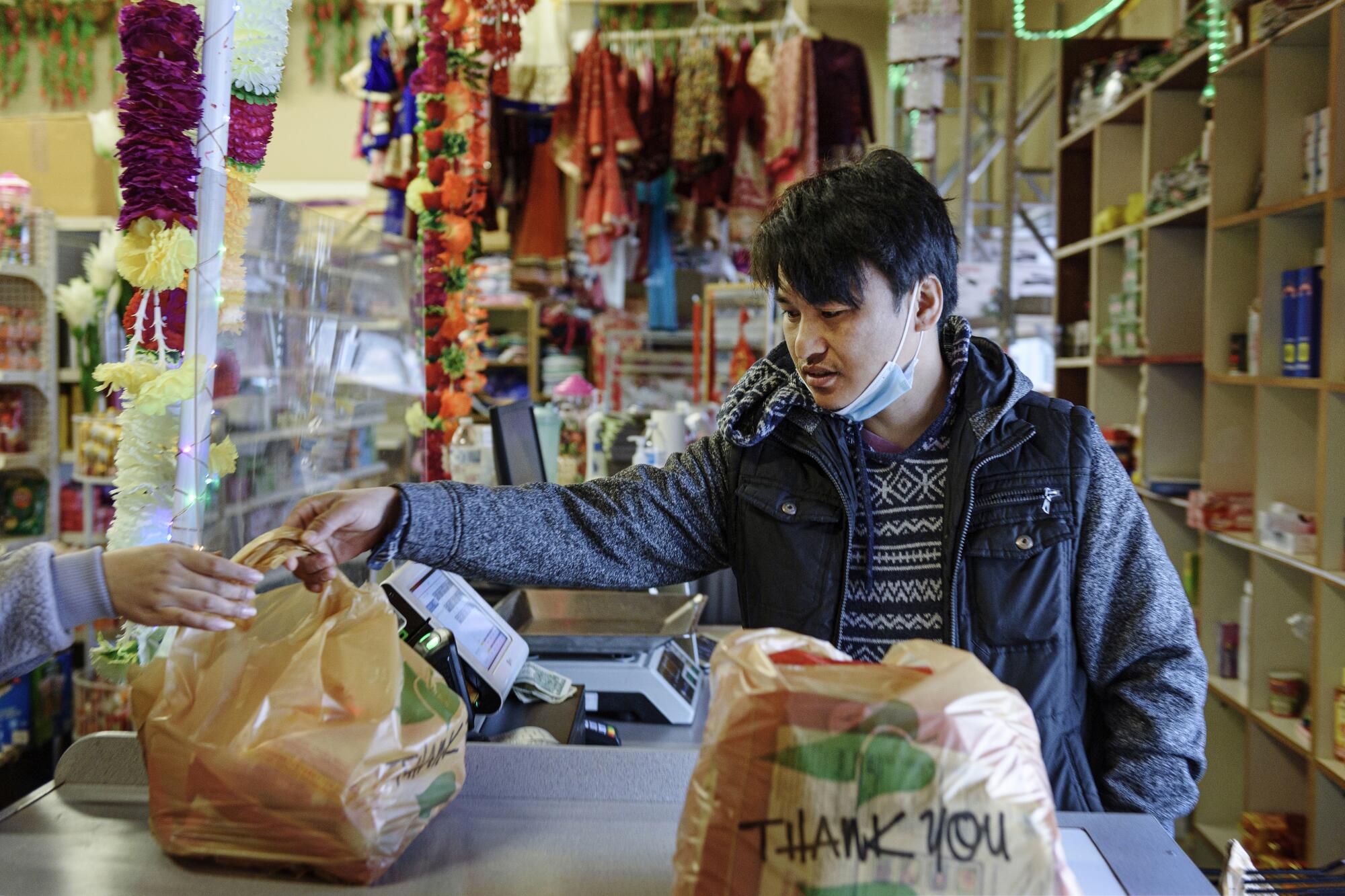 A man behind a counter hands grocery bags to a customer