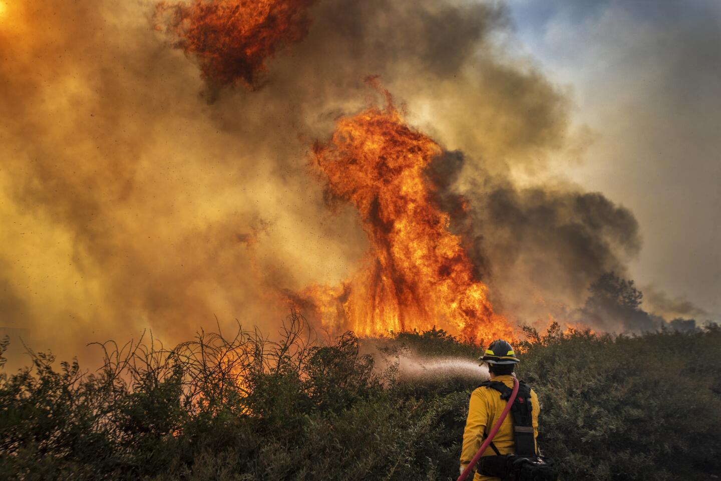 A firefighter sprays water toward a wall of flames