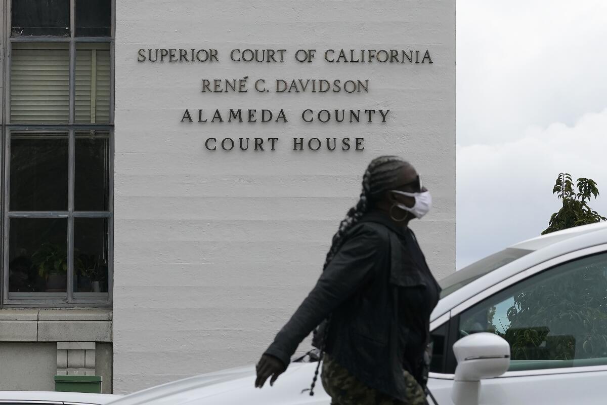 FILE - In this March 9, 2021, file photo, a pedestrian wears a face mask while walking across the street from the Alameda County Court House during the coronavirus outbreak in Oakland, Calif. The official COVID-19 death count in Alameda County, in the San Francisco Bay Area, fell from 1,634 to 1,223 after officials changed the criteria for fatalities to match state and national definitions, the county's public health department said in a news release. The county will now only report deaths as coronavirus-related fatalities when people died as a direct result of COVID-19, or had the virus as a contributing cause of death as well as people for whom COVID-19 could not be ruled out as a cause of death. (AP Photo/Jeff Chiu, File)