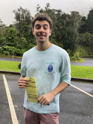 A man stands in a parking lot holding a paper citation.