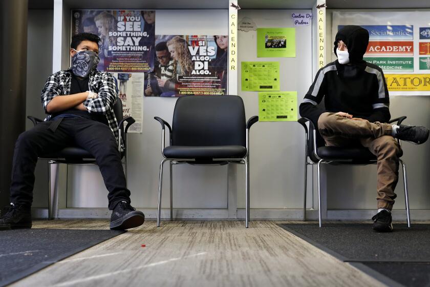 HUNTINGTON PARK-CA-MARCH 26, 2020: Tenth grade students Erik Garcia, 15, left, and Fredy Rubio, 16, wait to pick up laptops at Linda Esperanza Marquez High School in Huntington Park, for school work at home, on Thursday, March 26, 2020. (Christina House / Los Angeles Times)