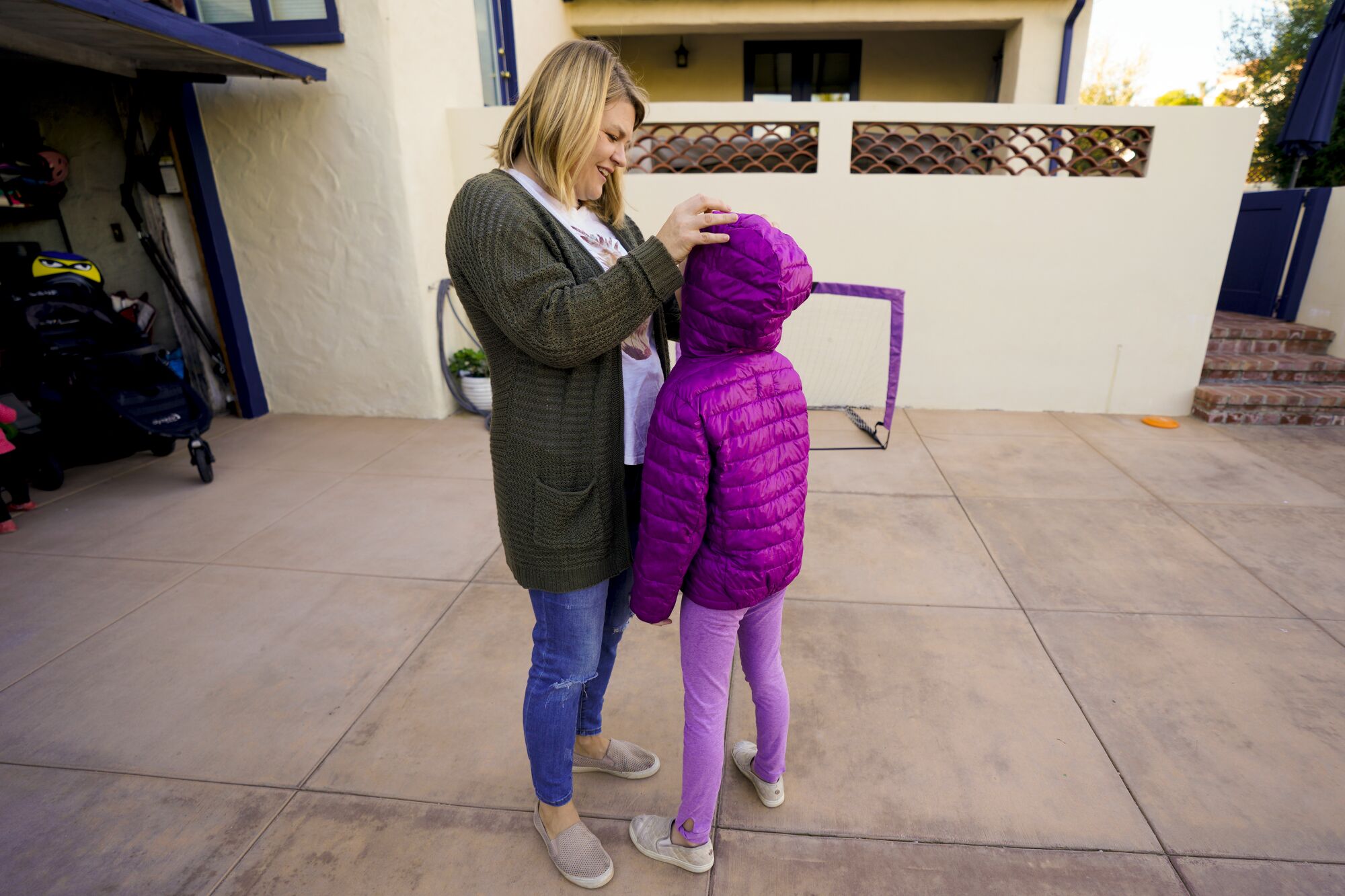 A blonde woman stands in front of an open garage, her hands on the head of a child who stands with her back to the camera.