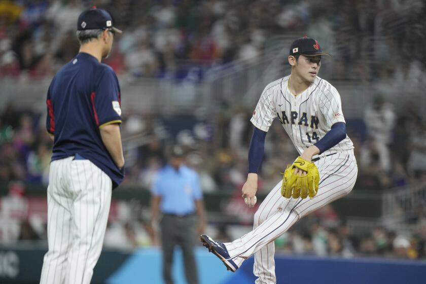 Japan pitching coach Masato Yoshii, left, watches Japan pitcher Roki Sasaki throw a pitch after he was checked out by a trainer during the second inning of a World Baseball Classic game against Mexico, Monday, March 20, 2023, in Miami. (AP Photo/Wilfredo Lee)