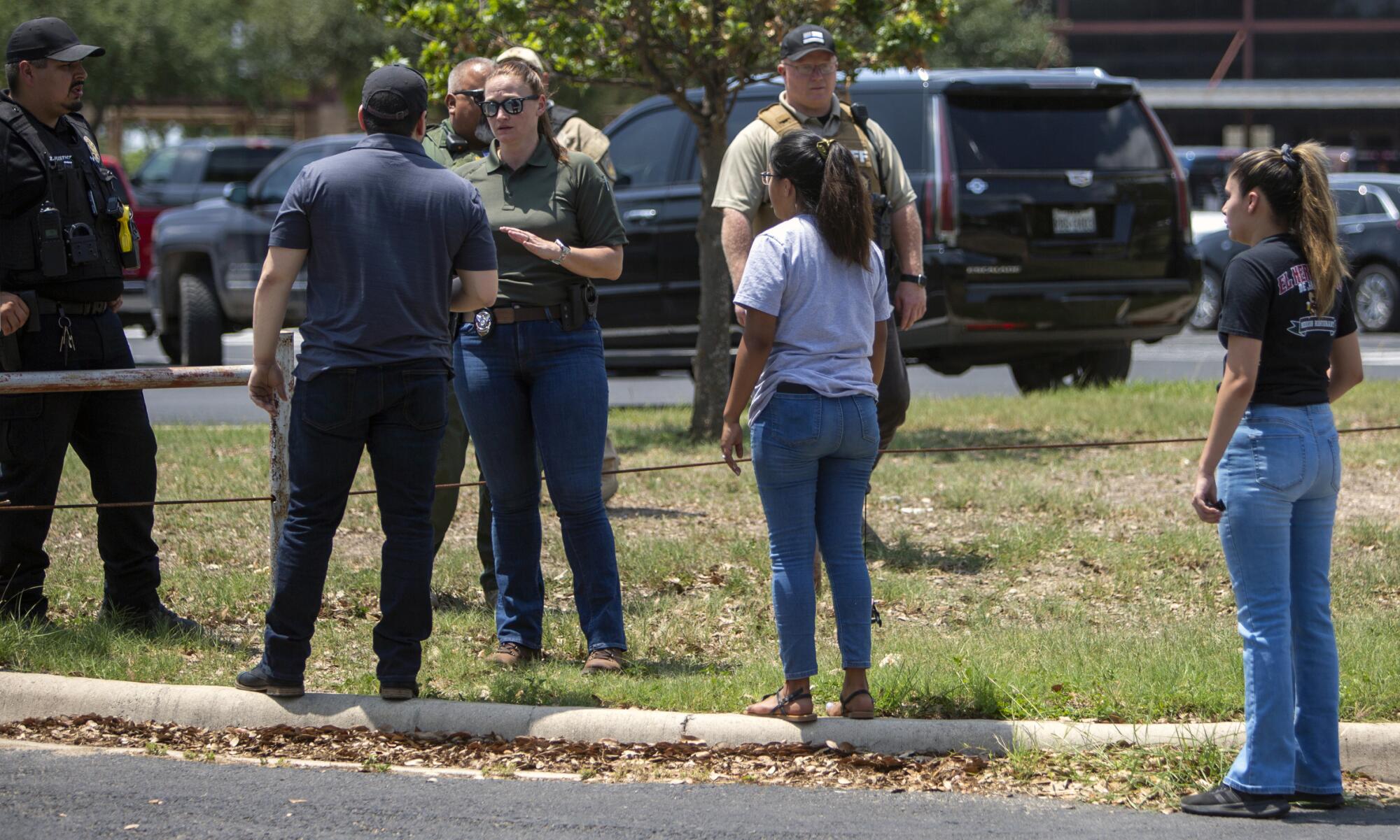 A woman in a green shirt and jeans standing near uniformed officers speaks to a man as two young women look on 