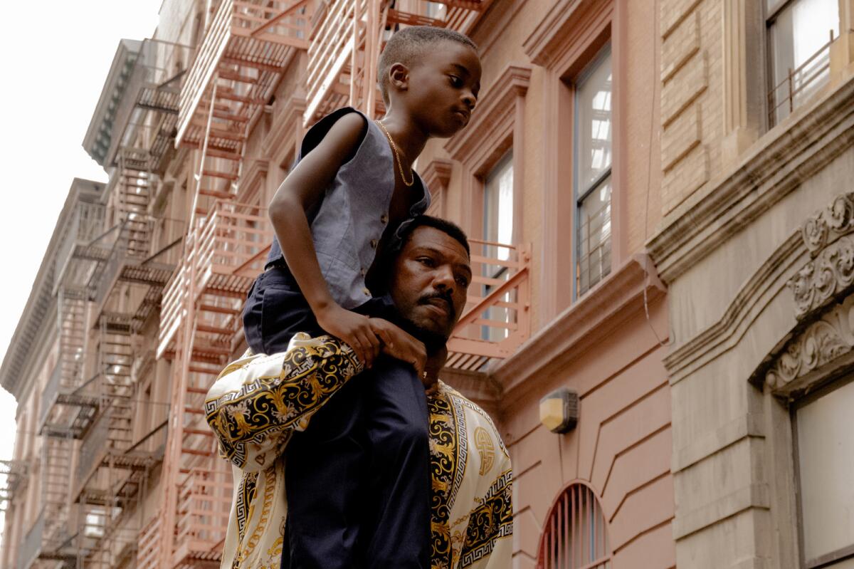 A man carries a boy on his shoulder in front of a row of  apartment buildings