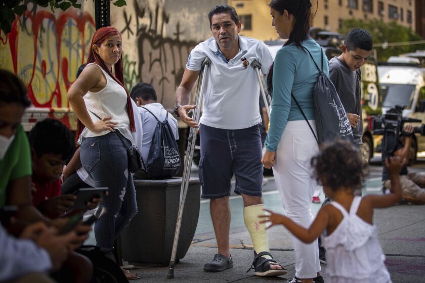 ARCHIVO - Eduardo García, de Venezuela, de pie con muletas, y rodeado de su familia afuera de la sede de Caridades Católicas, el 16 de agosto de 2022 en Nueva York. (AP Foto/Robert Bumsted, File)