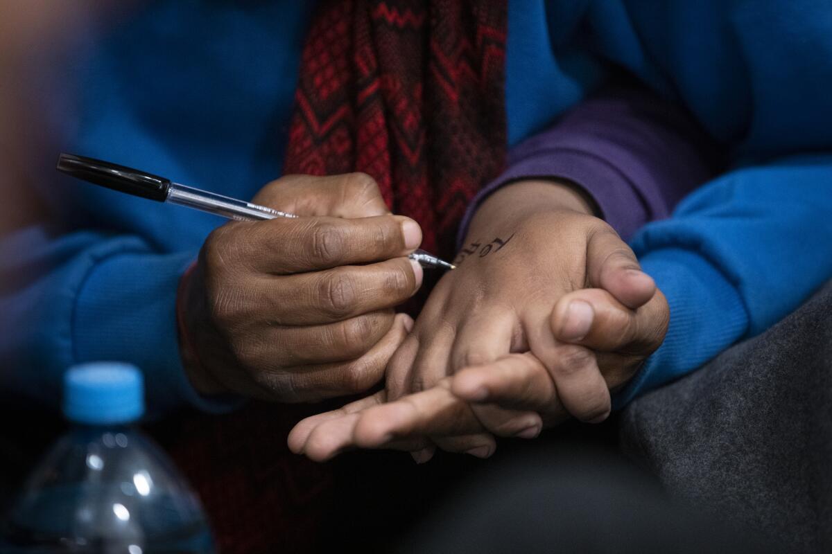 A closeup of a man using a pen to write on the back of a woman's hand, her fingers entwined with those of his free hand