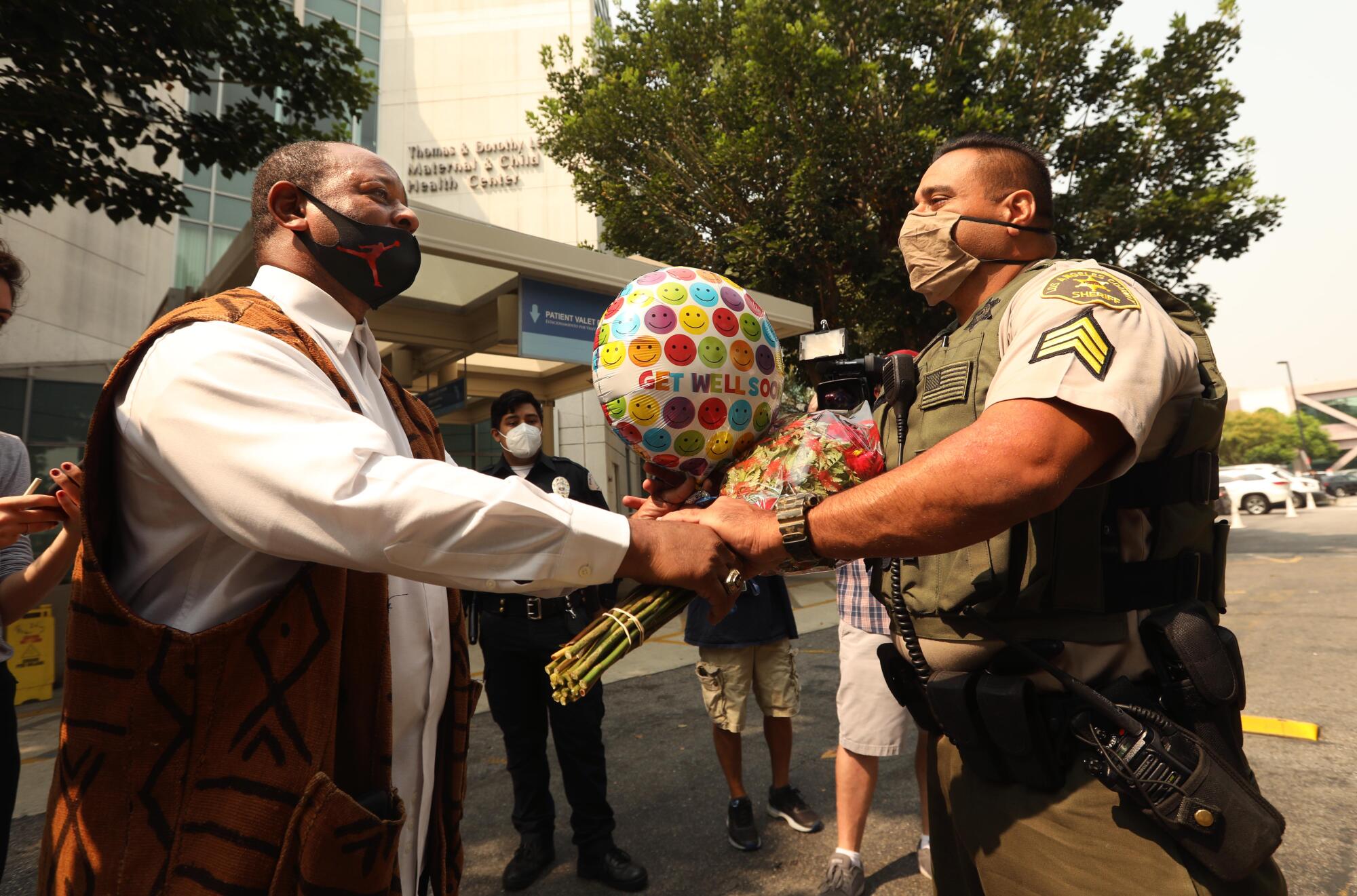 Activist Najee Ali, left, gives flowers to sheriff's Sgt. Larry Villareal