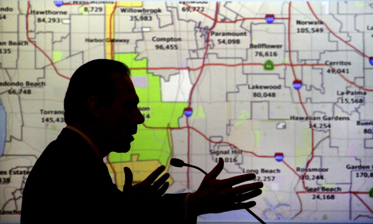 A person speaks in front of a screen showing legislative maps