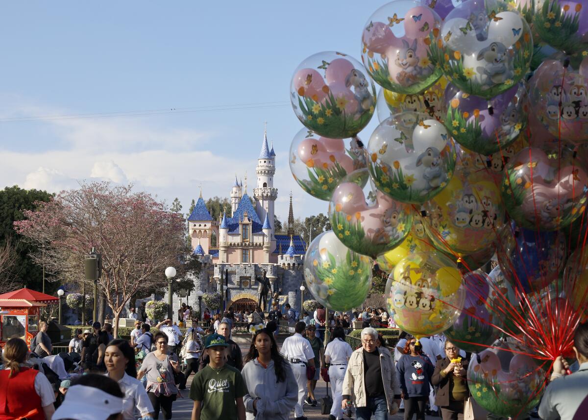 Balloons appear in the foreground as people walk to and from a fairy-tale castle.
