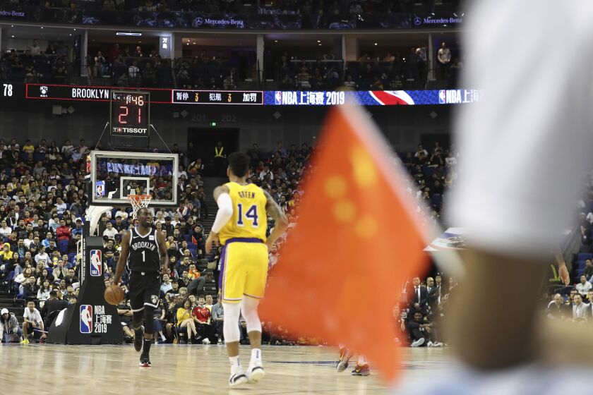 Brooklyn Nets' Theo Pinson, left, drives against Los Angeles Lakers' Danny Green near a Chinese national flag during a preseason NBA basketball game at the Mercedes Benz Arena in Shanghai, China, Thursday, Oct. 10, 2019. In response to the NBA defending Daryl Morey's freedom of speech, Chinese officials took it away from the Los Angeles Lakers and Brooklyn Nets. All of the usual media sessions surrounding the Lakers-Nets preseason game in Shanghai on Thursday — including a scheduled news conference from NBA Commissioner Adam Silver and postgame news conferences with the teams — were canceled. It was the latest salvo in the rift between the league and China stemming from a since-deleted tweet posted last week by Morey, the general manager of the Houston Rockets. (AP Photo)
