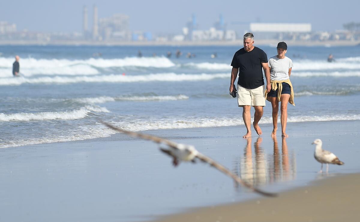 People walk along the shore in Newport Beach last weekend after Gov. Gavin Newsom closed all of Orange County's beaches to slow the spread of the coronavirus.