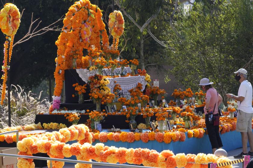 Unas personas observan una ofrenda colocada por la festividad del Día de los Muertos en Los Ángeles, el jueves 29 de octubre de 2020. (AP Foto/Damian Dovarganes)