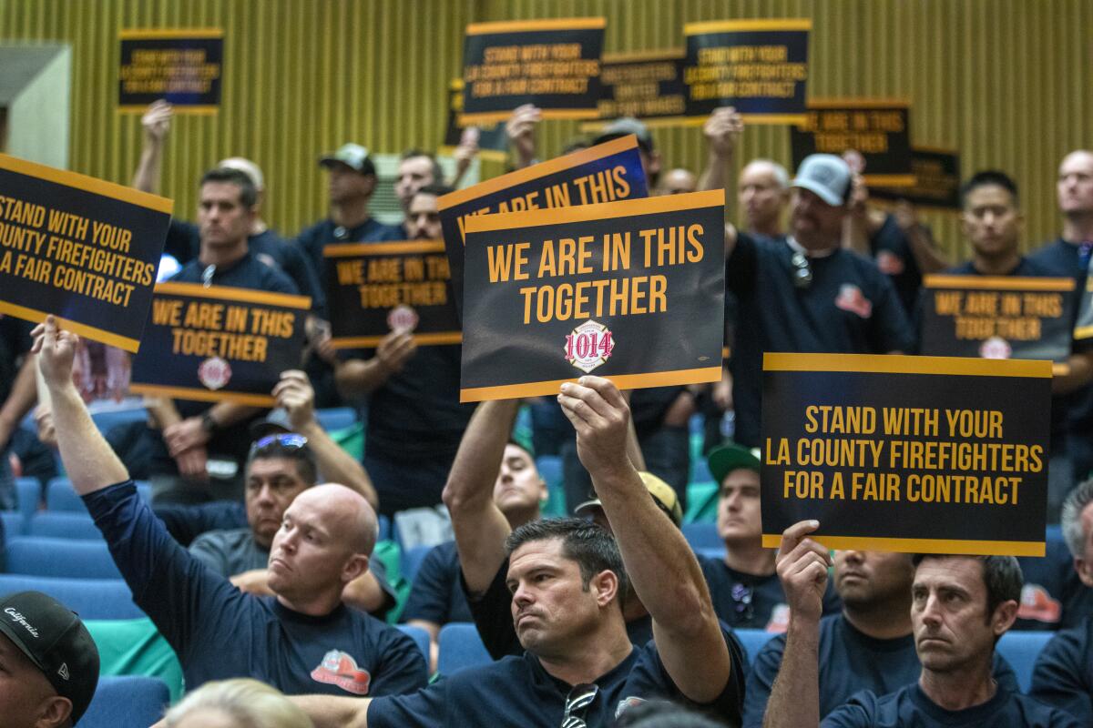 Firefighters and paramedics hold up signs at a county Board of Supervisors meeting on Nov. 15.