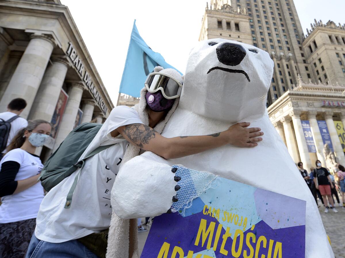 An activist in goggles and mask embraces a decorative polar bear at a protest. 
