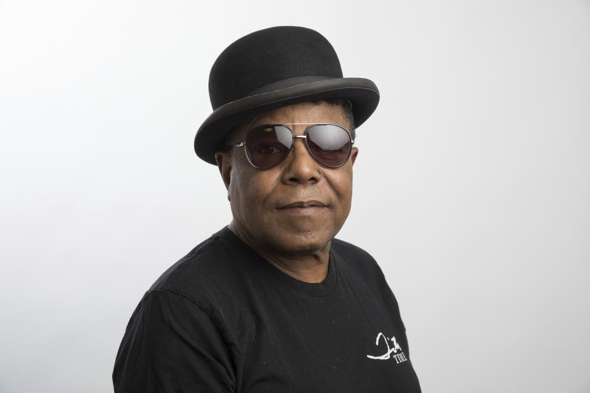 Tito Jackson posing in a black T-shirt, aviator sunglasses and a bowler hat