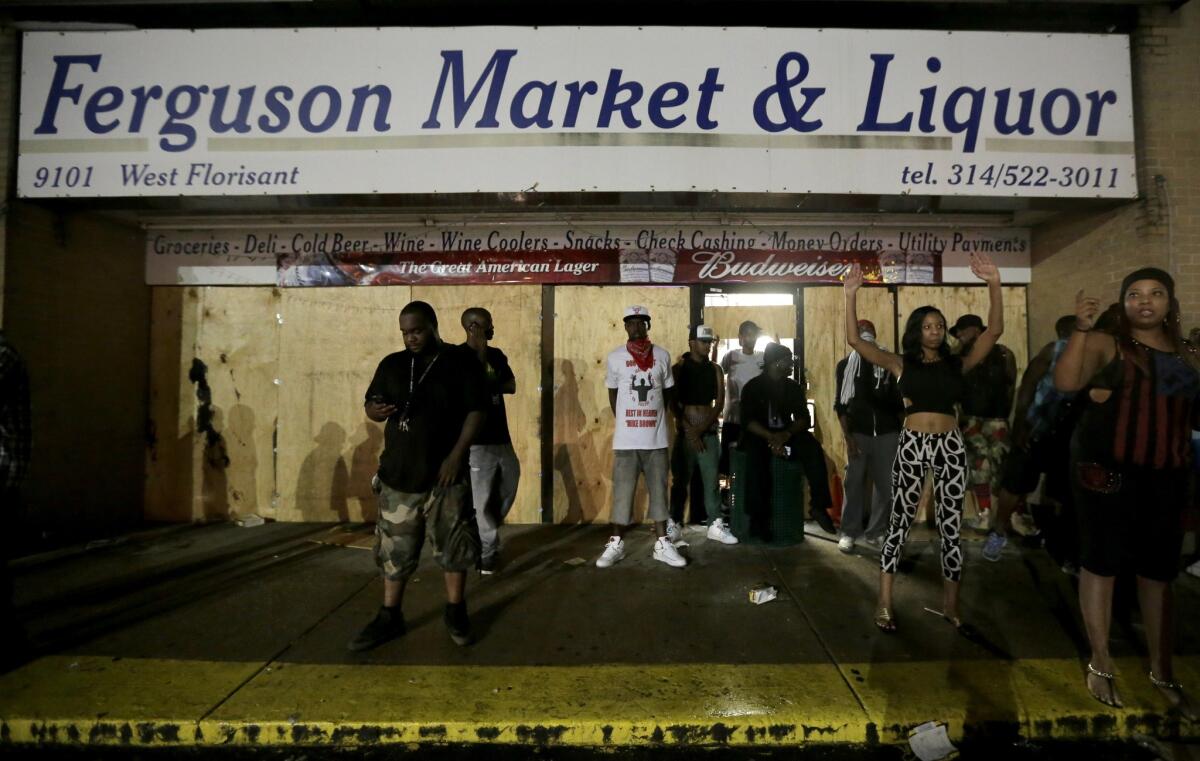Demonstrators stand in front of a Ferguson, Mo., convenience store after it was looted early Saturday.