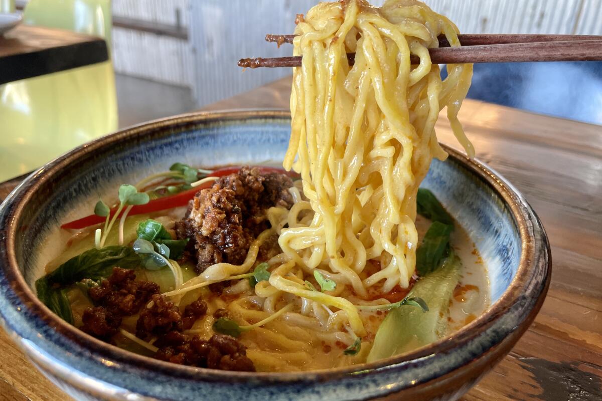 chopsticks hold up noodles out of a bowl of ramen