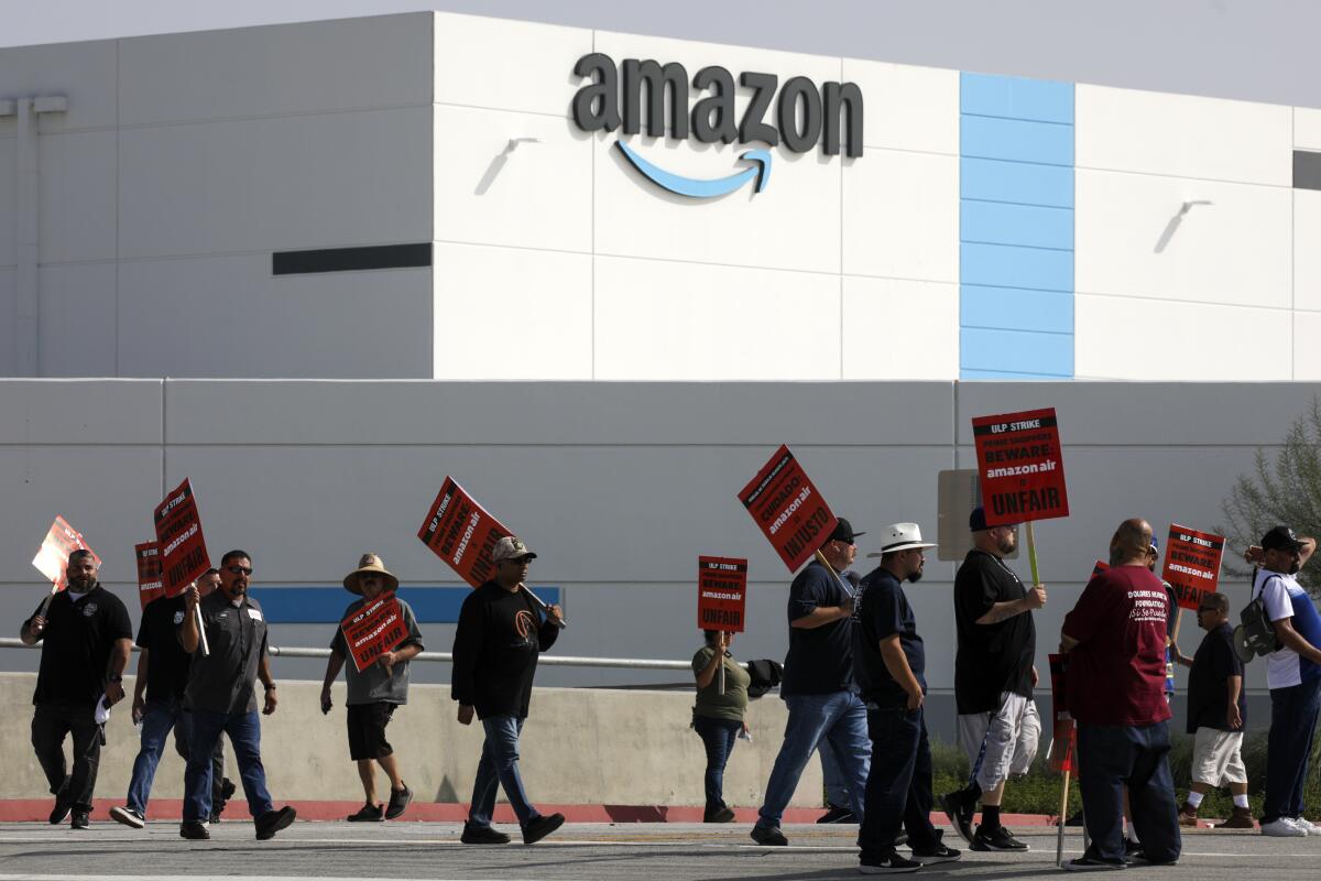 Workers carrying signs picket outside an Amazon warehouse