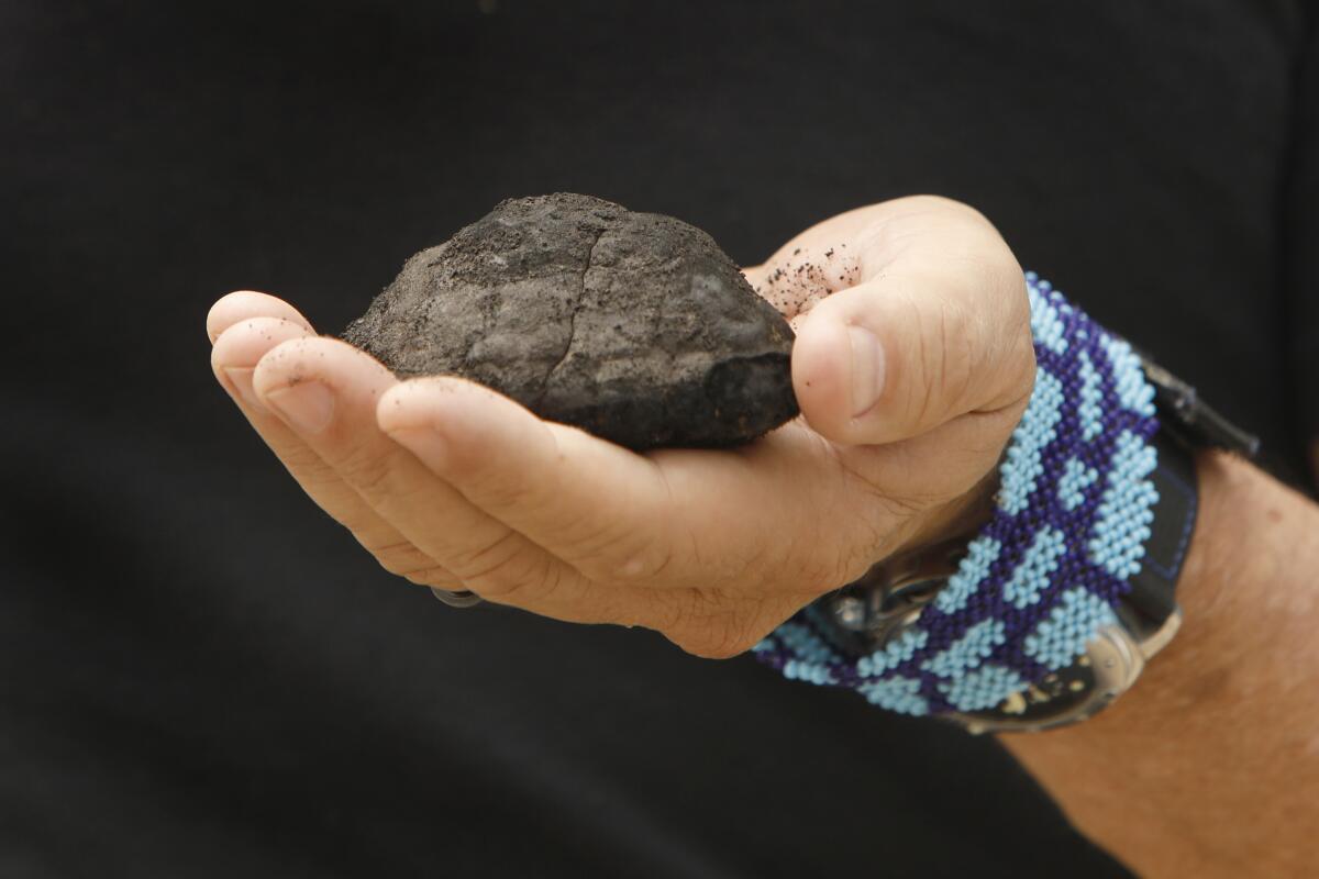 A metallic nodule brought up from the seafloor rests in a man's upturned hand.