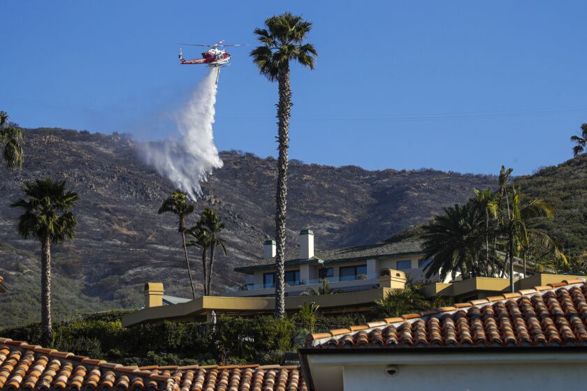 Laguna Beach, CA - February 10: A helicopter working the Emerald fire makes a water drop on the homes above Irvine Cove on Thursday, Feb. 10, 2022 in Laguna Beach, CA. (Irfan Khan / Los Angeles Times)