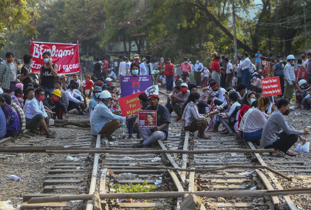 Demonstrators, some with signs, sit on railway tracks in Myanmar.