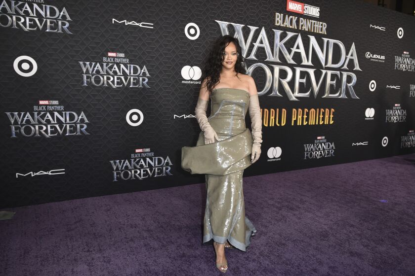 A woman in a shiny gown poses on a black carpet for a movie premiere