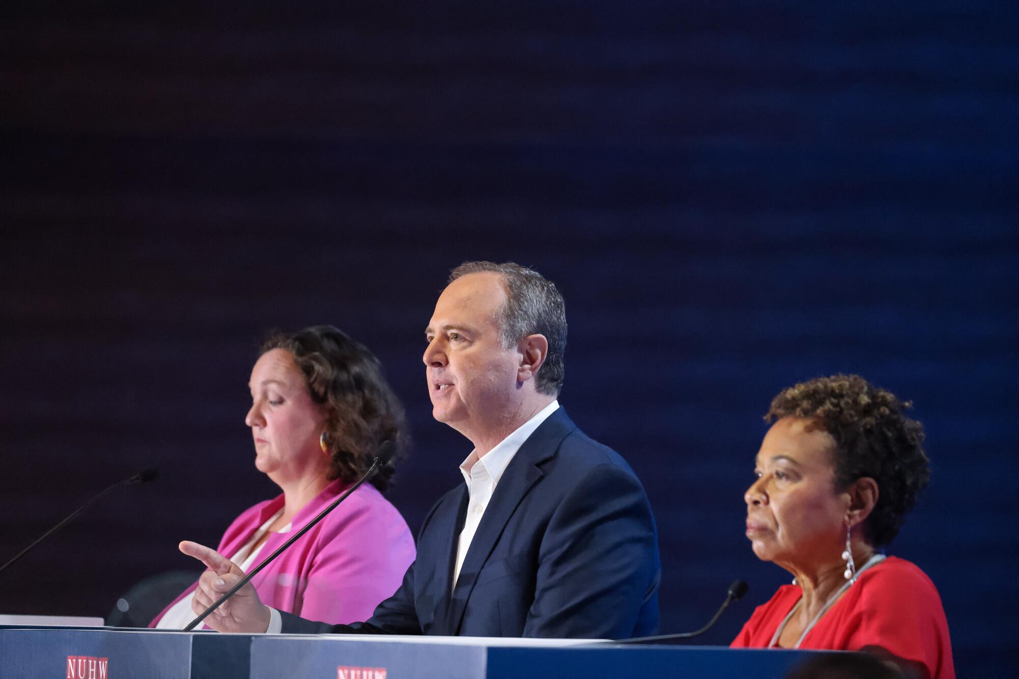 Three candidates stand before lecterns during a debate.