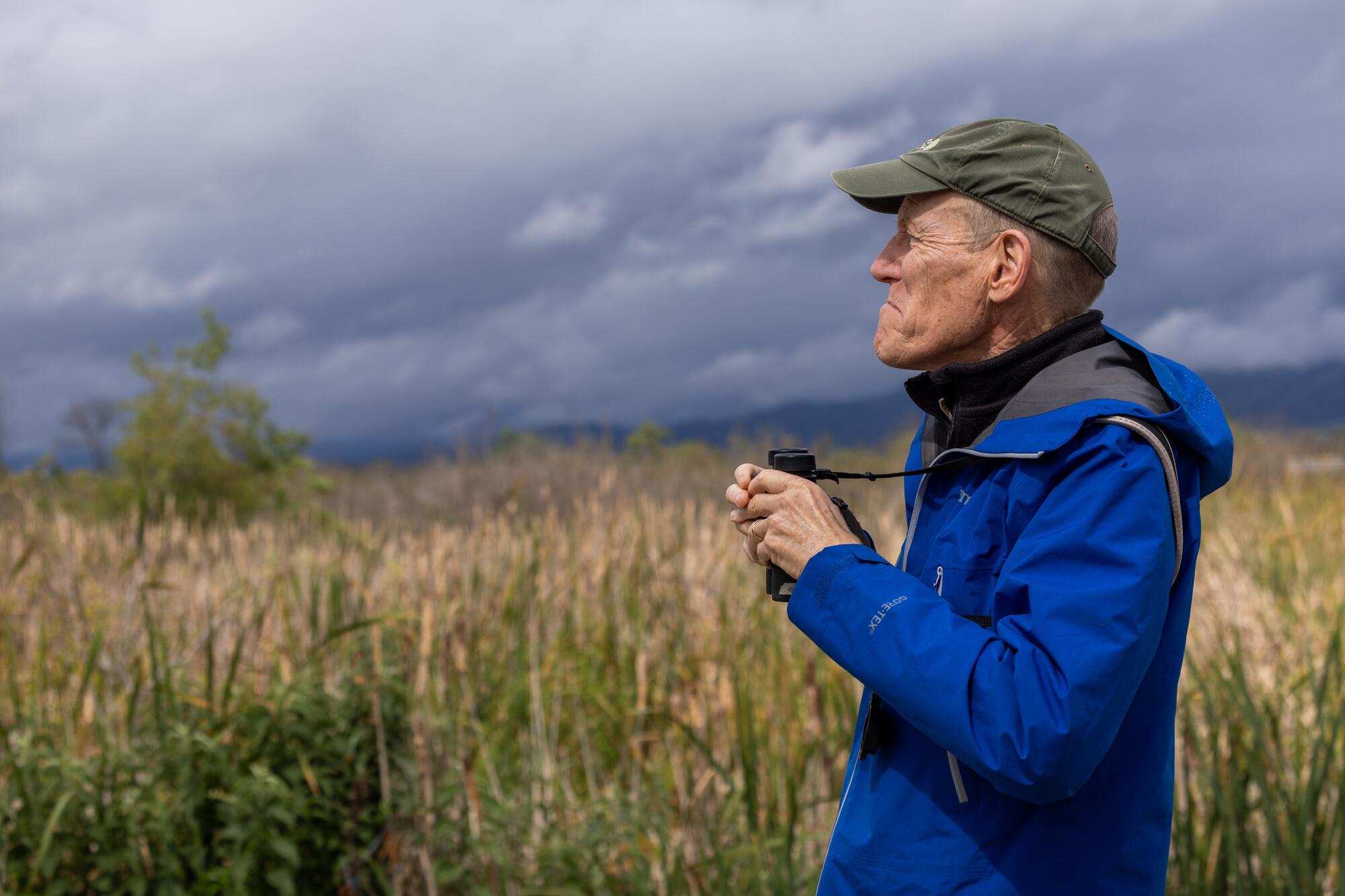 A man holds binoculars as he observes a wetland.