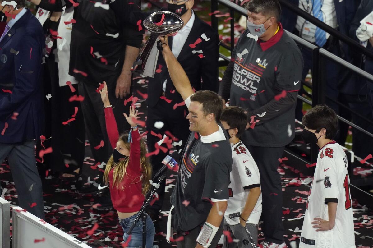Tom Brady stands amid confetti, with his young daughter and two sons around him, holds up a trophy.