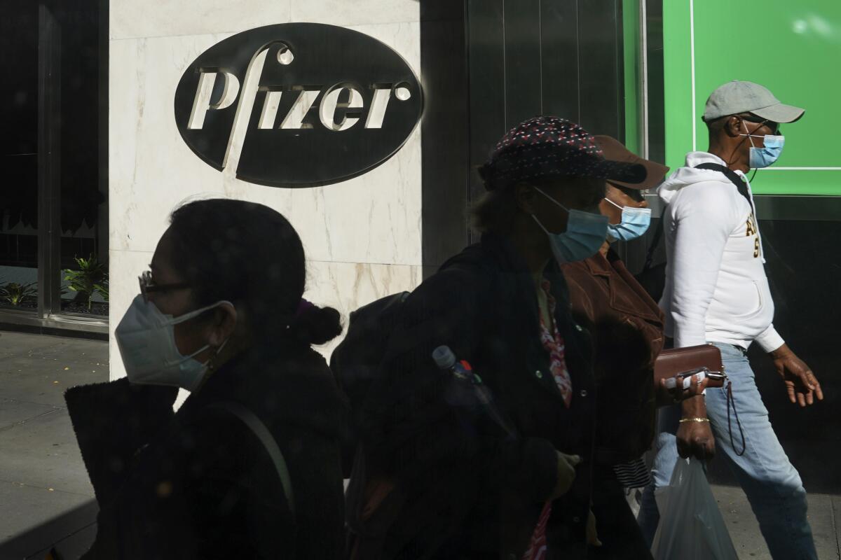 Pedestrians walk past Pfizer world headquarters in New York on Monday Nov. 9, 2020. Pfizer says an early peek at its vaccine data suggests the shots may be 90% effective at preventing COVID-19, but it doesn't mean a vaccine is imminent. (AP Photo/Bebeto Matthews)