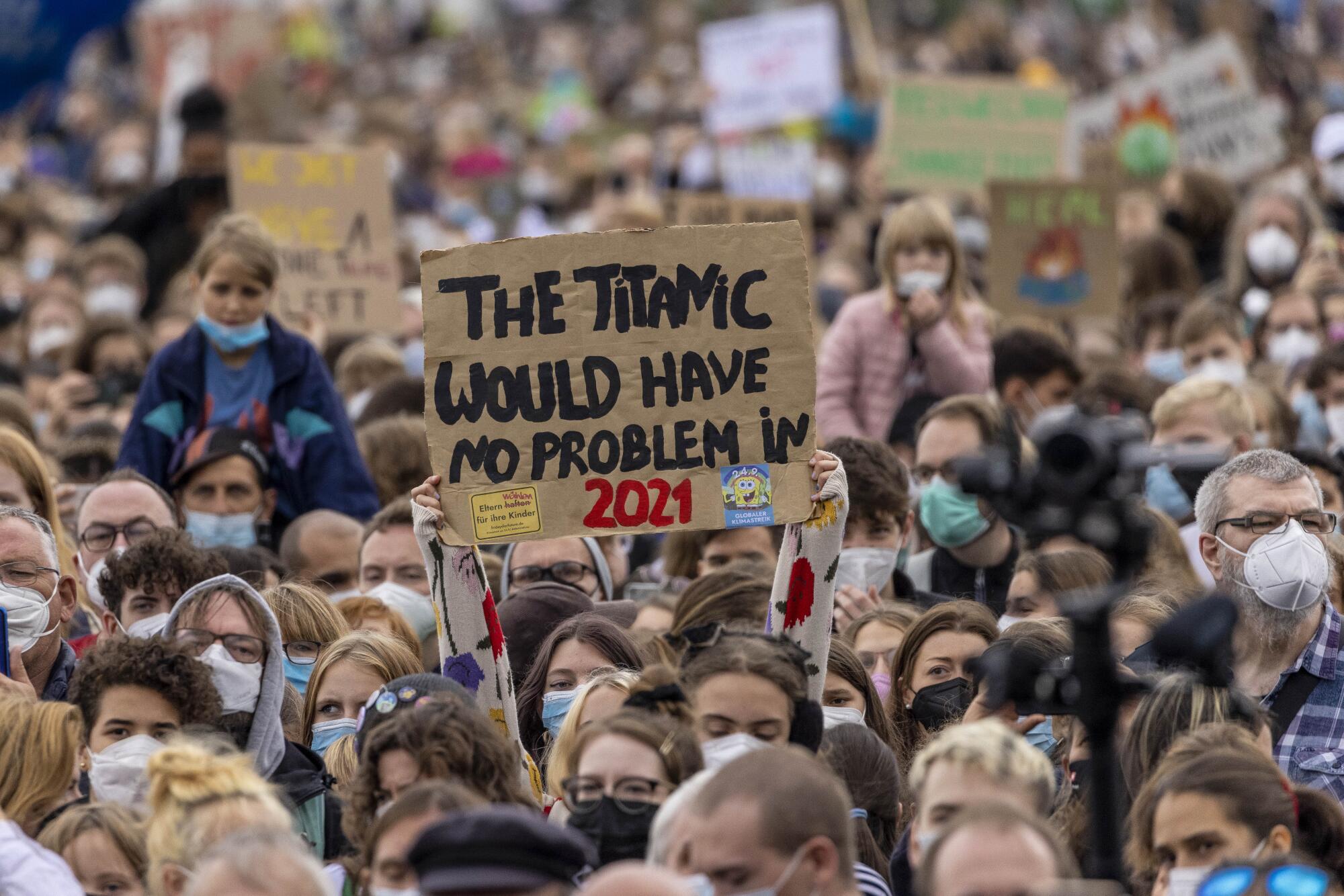 In a sea of people, a sign is held overhead that reads, "The Titanic would have no problem in 2021." 