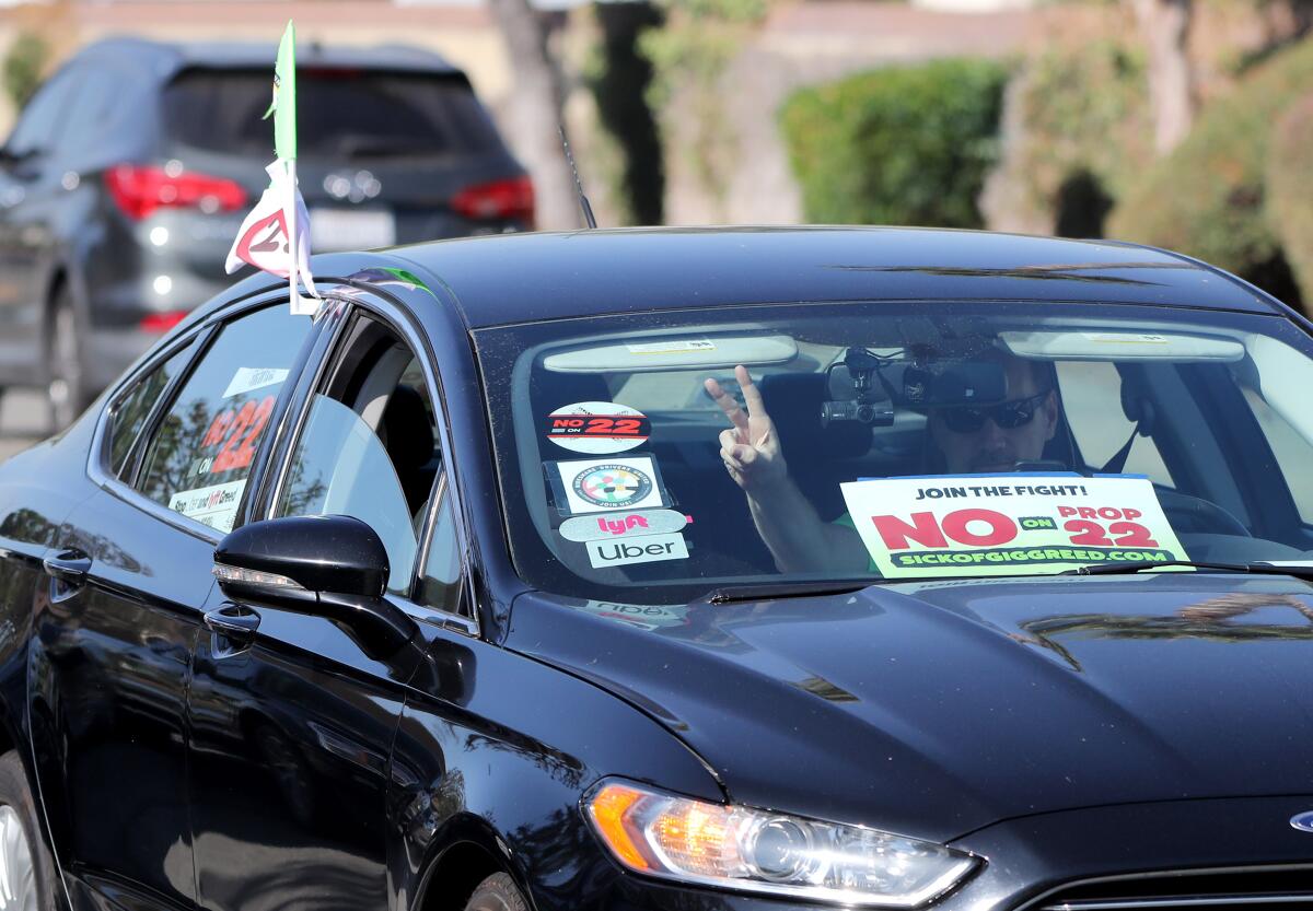 A driver with Uber and Lyft stickers and a "No on Prop 22" sign on his window pulls up at a rally in Orange.