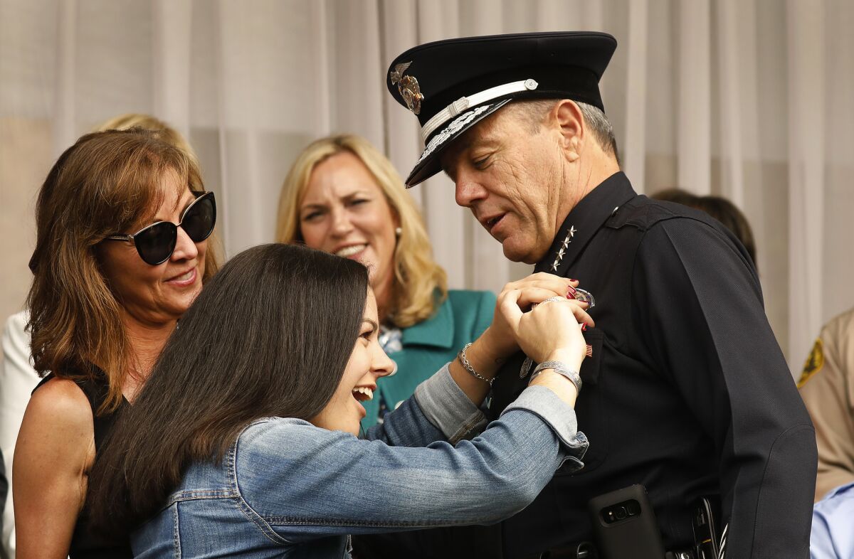 Haley Moore, 18, daughter of the new LAPD Chief Michel Moore, places his new badge as his wife, Cindy Moore, left, watches at the swearing-in ceremony of Los Angeles' 57th police chief.