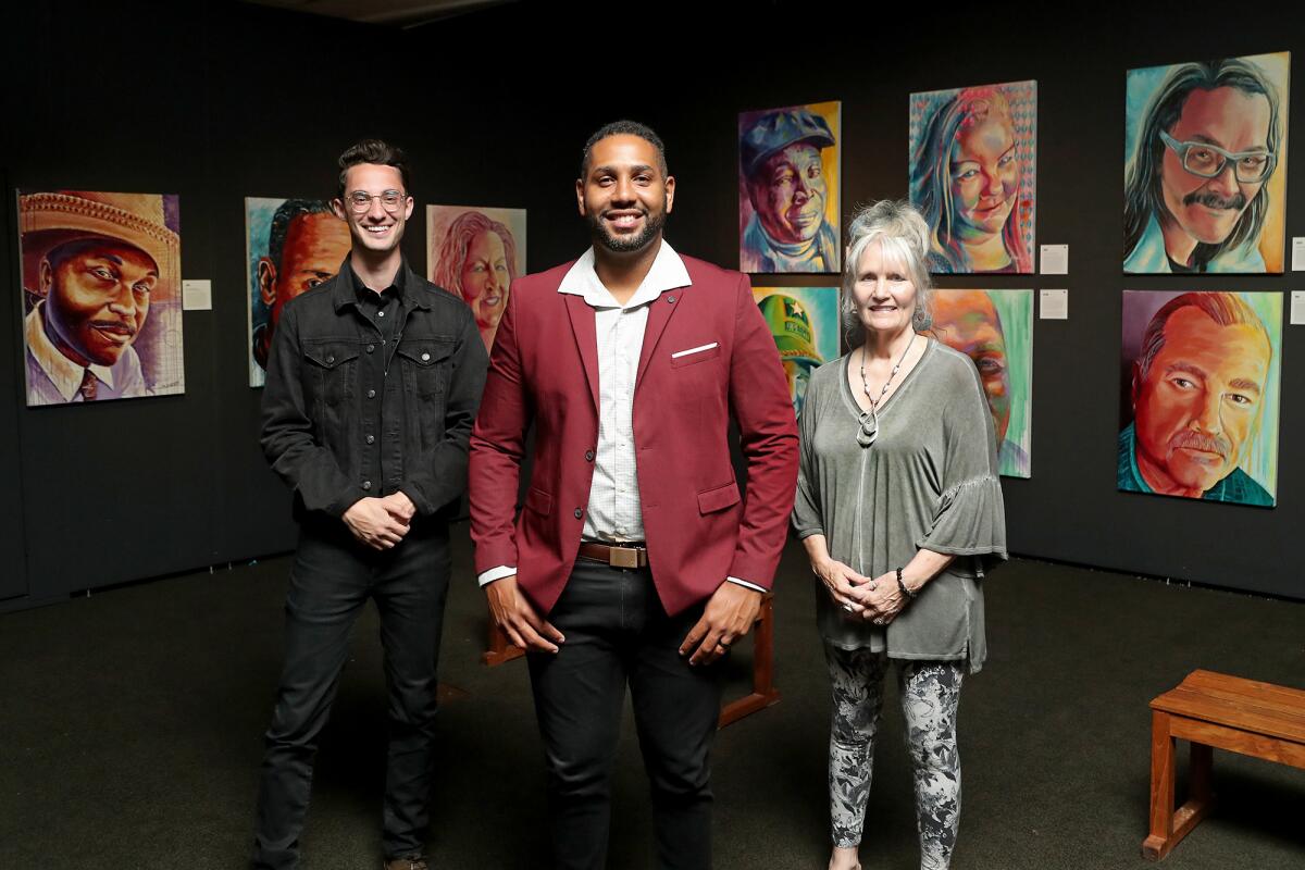 Artists pose for a portrait in front of a display of paintings in a gallery