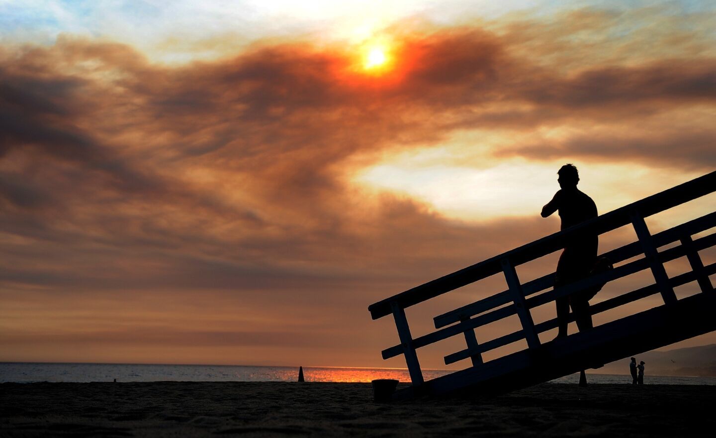 As smoke billows from the Springs fire, a lifeguard keeps an eye on swimmers at Zuma Beach.