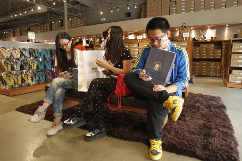 Bam Wang, left, Zhe Chen, middle, and Shuai Wu wait for a friend shopping at the UGG store at the Desert Hills Premium Outlets in Cabazon. The U.S. is the top destination for world travelers, according to a new survey.