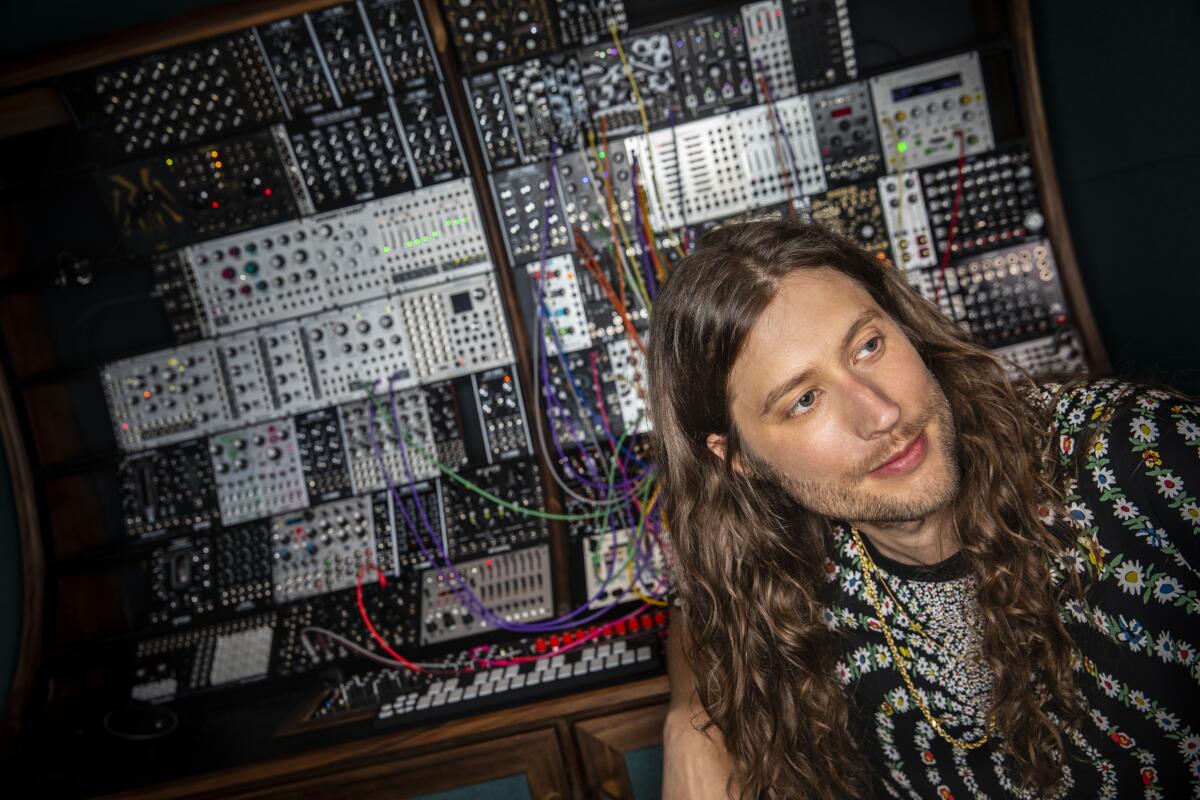 Ludwig Göransson, who wears long hair and a psychedelic shirt, sits before sound panels inside a recording studio
