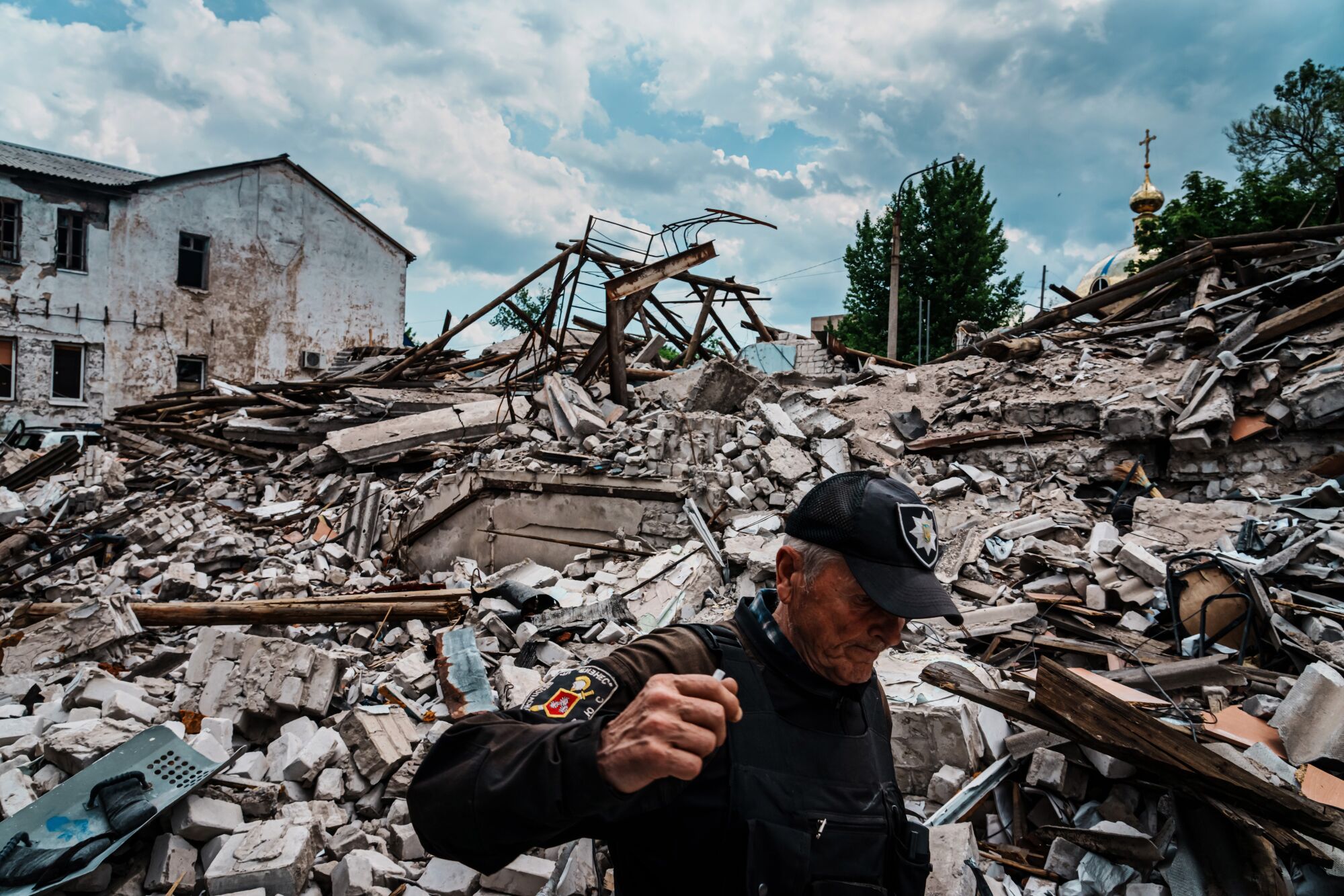A man in dark cap and uniform walks past a mountain of rubble 