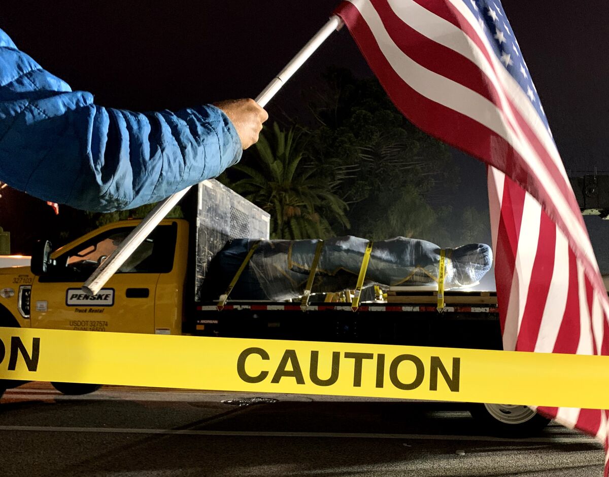 Aidan Wood holds an American flag as the statue of Father Junipero Serra is removed from in front of Ventura City Hall.