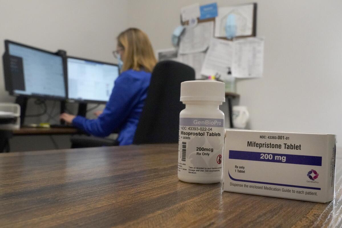 A woman works in an office while a container of medication sits on a table nearby.