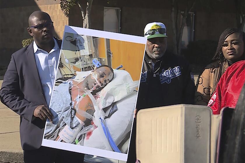 In this photo provided by WREG, Tyre Nichols' stepfather Rodney Wells, center, stands next to a photo of Nichols in the hospital after his arrest, during a protest in Memphis, Tenn., Saturday, Jan. 14, 2023. (Jordan James/WREG via AP)