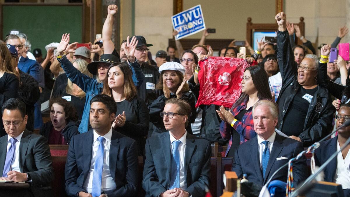 Port of L.A. officials sit in the front row as dockworkers and their supporters cheer the Los Angeles City Council's decision to veto a permit for Maersk to introduce driverless electric cargo handlers at the Port of L.A.