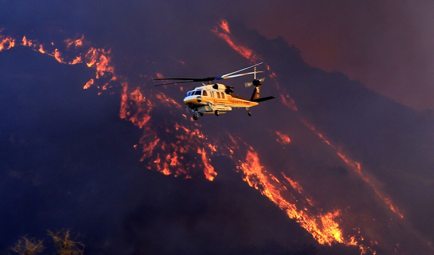 A water-dropping helicopter flies over the Colby fire burning in the Angeles National Forest.