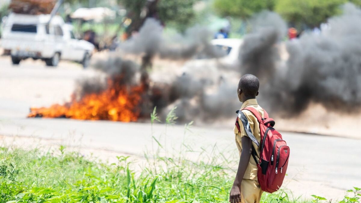 A student looks at a burning barricade during a demonstration Monday in Bulawayo after the president announced he was doubling gas prices.