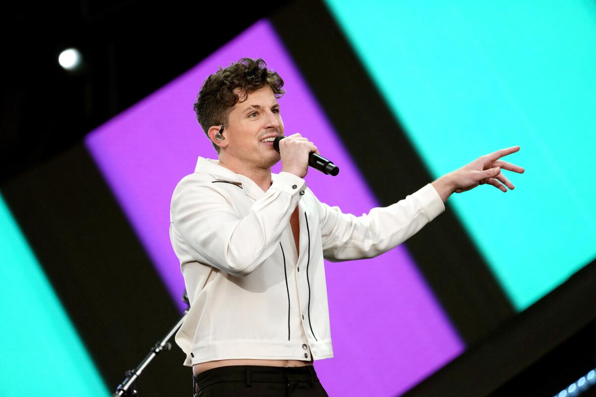 A man wearing a white button-up shirt and black pants sings into a microphone while onstage.