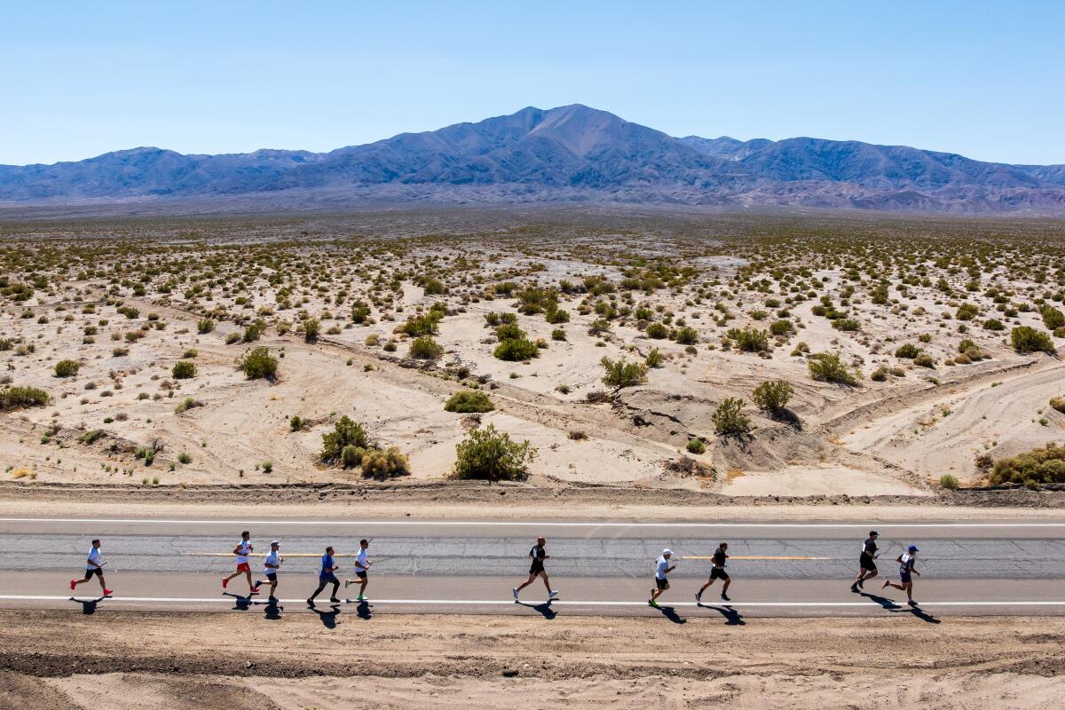 Runners on a desert road with mountains behind them.